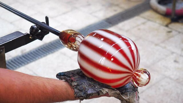 Hands cut melted glass with shears. Art and craft worker molding glass with wet newspaper while blowing artist piece i factory. Traditioal Czech glass 