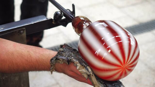 Art and craft worker shaping glass with mould from wet newspaper. Red white stripped glass art piece in skilled hands of glassblower master. 