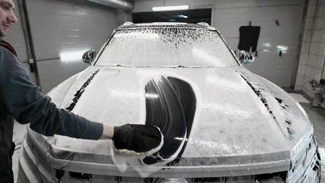 Man washing the car bonnet after shampooing the bodywork wiping the car surface with a special cleaning glove.