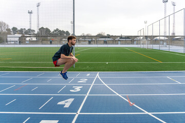 Fototapeta premium Hard working young runner boy doing warm-up in blue running track.