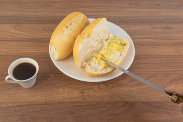 Brazilian Wheat Baked two French Bread and coffee, on wooden table and buttering bread - perspective view.