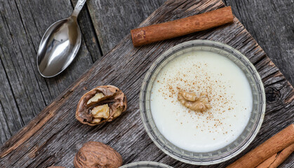 Pudding in glass bowl with cinnamon and walnut on rustic table, milk dessert