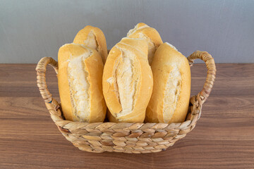Brazilian Wheat Baked French Bread, in straw basket on wooden table and gray background - perspective front view.