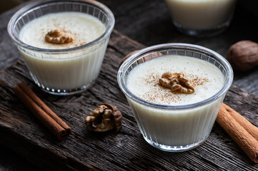 Pudding in glass bowl with cinnamon and walnut on rustic table, milk dessert