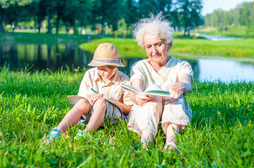 Attractive grandmother with her grandson are learning school assignments outdoors together. A boy...