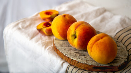 Peaches on table in kitchen near window. Rustic minimalism food peach fruits with leaves on wooden board on tablecloth. Harvest of Ripe juicy peaches. Long web banner