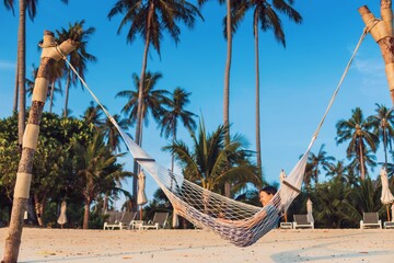 Obraz premium Asian traveler woman lying on the hammock on the beach in tropical resort hotel with Coconut tree and blue sky background.Travel in weekend holidays concept.