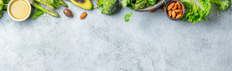 Fototapeta premium Vegetarian green ingredients on gray background. Vegetarian food - vegetables, greens, avocado, oil - health or cooking concept. Background layout with free text space