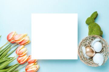 Naklejka na ściany i meble Easter decoration. Golden, white colour egg in basket with spring tulips, feathers on pastel blue background in Happy Easter decoration. Foil minimalist egg design with copy space.