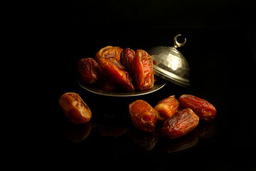 Dried palm date fruits in a silver bowl on black background