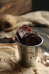 Homemade beef jerky seasoned with garlic, onion, pepper and salt. Jerky in a bucket on a wooden background