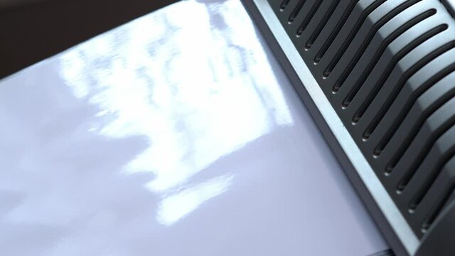 Close-up of a laminated white sheet of paper coming out of the laminator