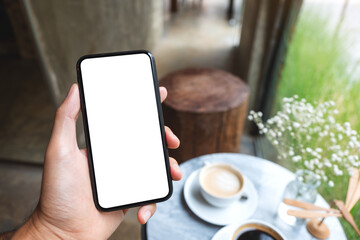 Mockup image of a hand holding and showing mobile phone with blank white screen in cafe