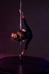 Graceful girl doing gymnastic exercise near pole in darkness