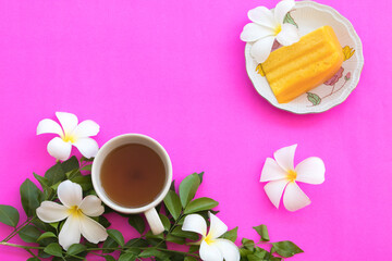 Obraz na płótnie Canvas dessert snack orange cake and hot coffee with flowers frangipani arrangement flat lay postcard style on background pink