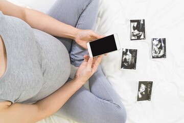 Top view of expecting pregnant woman in the bed with ultrasound scans and holding mobile phone, boy or girl, pregnancy and birth concept