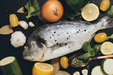fish with lemon and vegetables. Delicious fresh fish on black dark background. Fish with aromatic herbs, spices and vegetables on a black table. healthy food, diet, cooking concept. Prepare fish