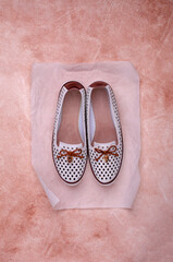 Light women's shoes with a bow and perforation on a brown background.