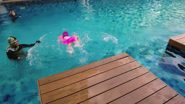 Toddler girl jumping into swimming pool from the deck and holding breath for seconds. Active kids having fun together. Footage may contain noise due to low light.
