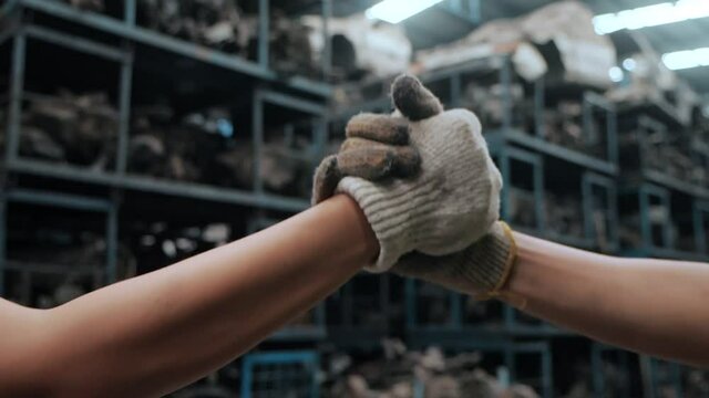 Close up of Handshake two workers or high five wearing working gloves at industrial factory background, Teamwork partnership industrial concept. Sensitive focus, Slow motion.