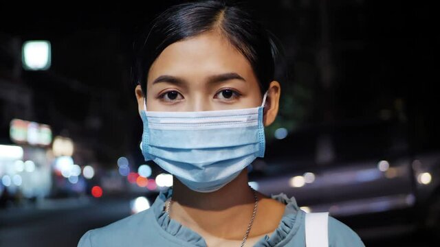Asian woman wearing a dustproof mask on the street at night.