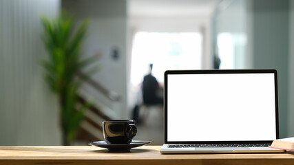 Mock up computer laptop and coffee cup on wooden table with blurred living room background.