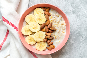 oatmeal with banana, almonds nuts in pink bowl, glass of milk, napkin on gray concrete background Top view Healthy breakfast or lunch Natural ingredients Rustic style