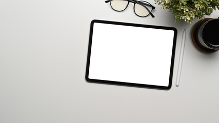 Top view of digital tablet with empty screen, glasses, plant and coffee cup on white office desk.