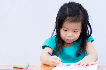 Asian girl is studying art. Child paint with color wooden. Pupil do crafts on drawing books. Children wear green clothes. Black-haired kids enjoyed drawing. Baby do homework on wooden table.