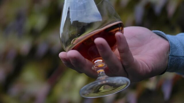Man's hand stir slowly cognac in the glass, slow motion.  
