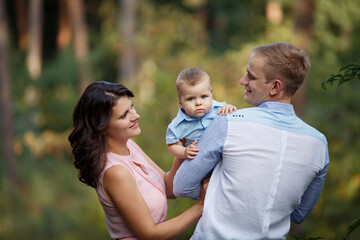 Happy family in a summer park. Family day. Little Boy with parents weared in casual green. Sunny summer day outdoors. Mother and father are holding their little son in hands. Walk in nature forest