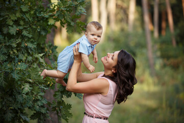 Obraz premium Happy family in a summer park. Family day. Little Boy with his mom in casual green outfit. Sunny summer day outdoors. Mother is holding her little son in hands. Walk in nature forest