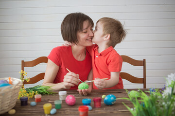 Obraz premium Mother and her son painting Easter eggs. Happy family preparing for Easter day