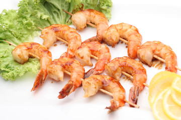 Grilled shrimp on a barbecue on wooden sticks with sauce and lemon.