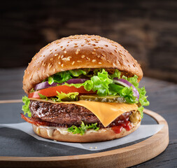 Delicious hamburger on a wooden table with a dark brown background behind. Fast food concept.