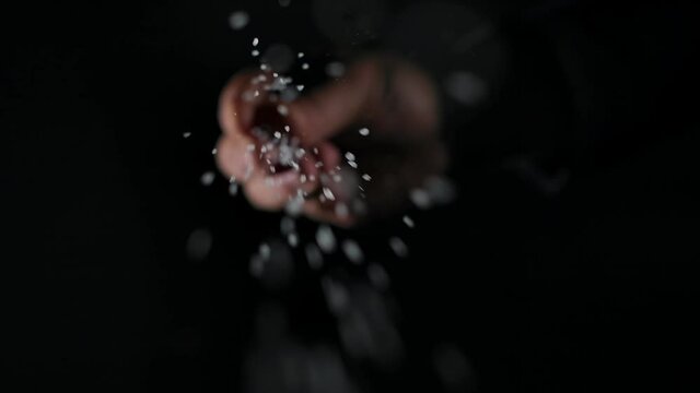 Person sprinkling salt. Chef sprinkles salt crystals over camera. black background, slow motion, close up
