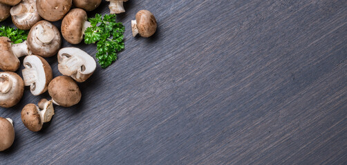 Brown colored edible mushrooms or cremini mushrooms on black table with herbs. Top view.