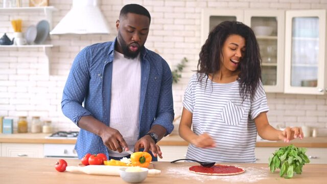 Happy multiethnic family in the kitchen having fun and cooking together, healthy food at home, young joyful couple have fun dancing and singing while set the table for breakfast