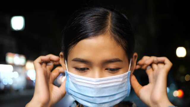 Asian woman wearing a dustproof mask on the street at night.