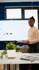 Black analyst using digital interactive whiteboard for presentation to a board of executives lawyers, in corporate meeting room, investors congratulating her clapping. Screen shows company growth data