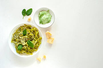 Green noodles with spinach and parmesan cheese in a white plate on a white table. Basic ingredients. Healthy food. View from above. Vertical photo.