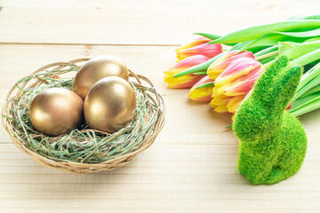 Easter eggs basket. Golden egg in basket with spring tulips, white feathers on wooden background in Happy Easter decoration. Traditional decoration in sun light.