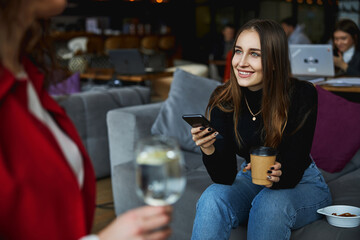 Charming young woman using cellphone and talking with colleague