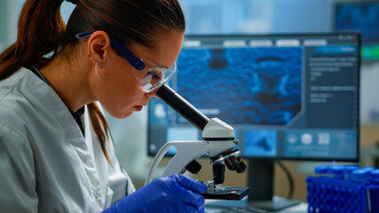 Portrait of scientist looking under microscope in medical development laboratory, analyzing petri...