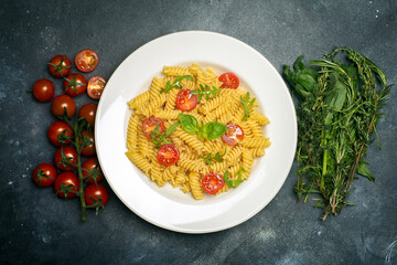 Food pasta on a dark background. Italian fusilli pasta with tomatoes, herbs and basil on a white plate. Healthy food concept.