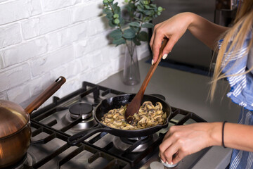 Fried mushrooms in a pan, cooked by a woman.