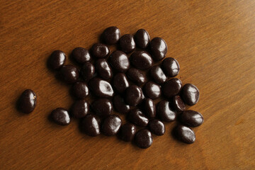 Dark chocolate drops on wooden background, top view, bitter raisin chocolate candy