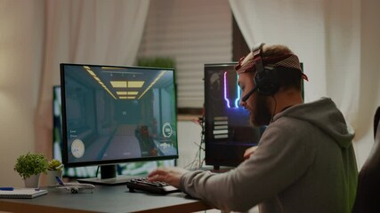 Cyber sport gamer wearing headphones playing first person shooter videogame participating in eSports tournament perforing at RGB prowerful personal computer. Pro cyber streaming gaming championship