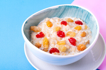 Porridge with milk, dried cherry and raisin in ceramic bowl against the colorful background. Breakfast meal. Kids food