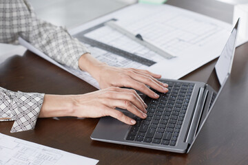 Close-up of businesswoman sitting at the table and typing on computer keyboard she working online at office